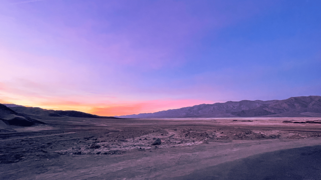 A serene twilight sky with shades of pink and blue over the vast expanse of Death Valley's desert landscape, as seen from the Gower Gulch Loop trail parking area.