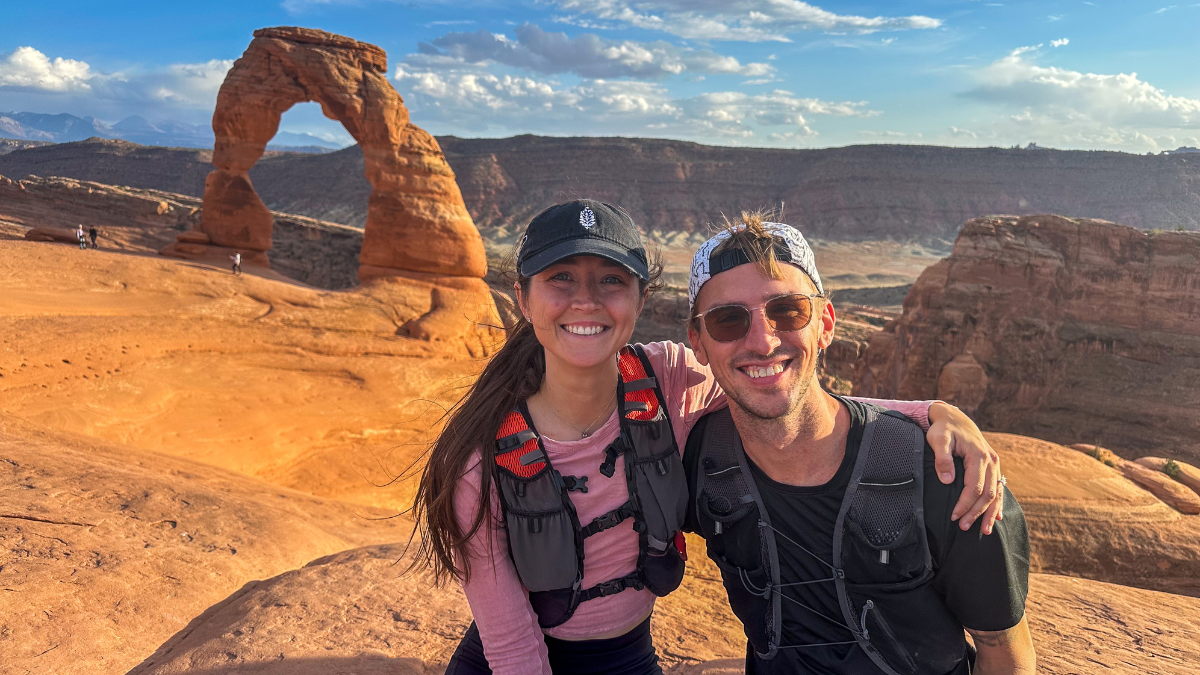 A man and woman pose for a picture in front of an arch in Arches National Park