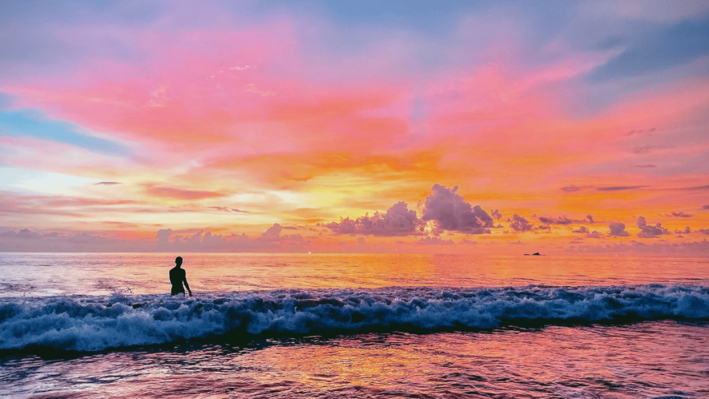 A breathtaking sunset at Bang Tao Beach with vivid pink and orange skies reflected in the water, silhouette of a person standing in the surf
