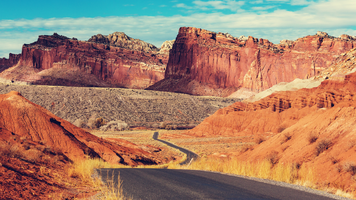 A winding paved road leads through a valley with colorful red rock formations and cliffs in Capitol Reef National Park.