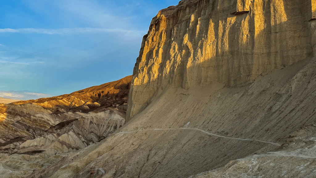 Sunset illuminates the rugged terrain of Gower Gulch, highlighting the textures and layers of the eroded hills with a hiking trail winding through the landscape.