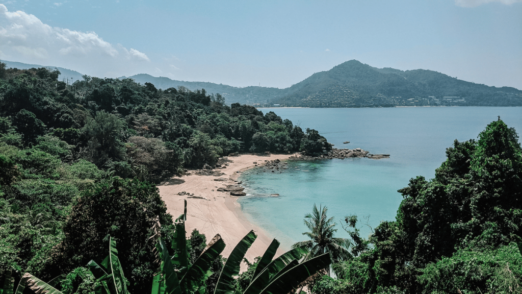 Secluded Laem Singh Beach in Phuket, surrounded by tropical greenery and clear blue waters, under a partly cloudy sky.