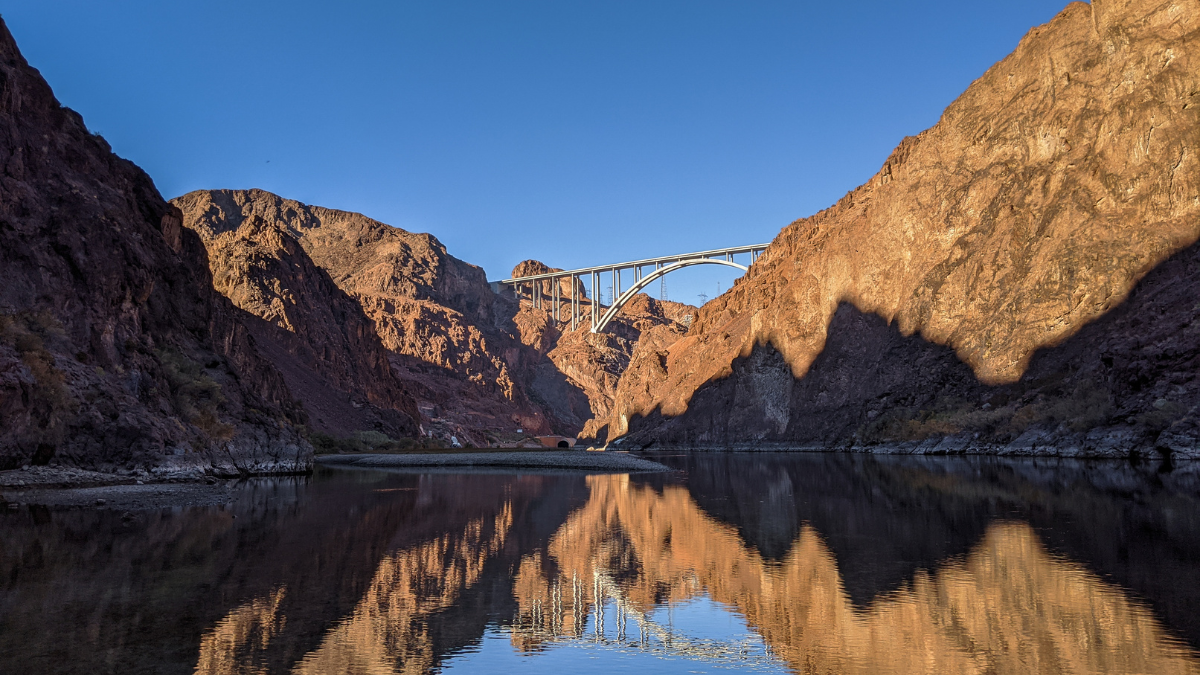 A graceful bridge arches over a river flowing through a steep canyon with rugged rock walls.