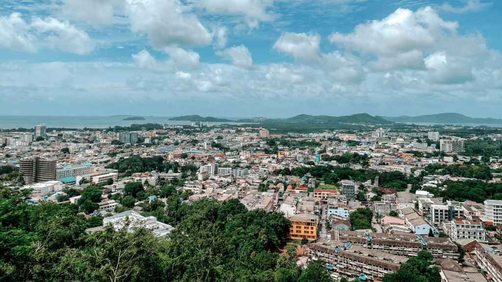 Aerial view of Phuket Town, showcasing the dense urban landscape with colorful buildings, streets, and the surrounding green hills.
