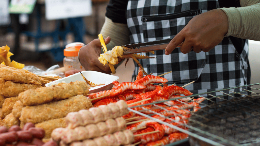 A street food vendor in Phuket expertly preparing grilled seafood, with skewers of shrimp and other delicacies on display.