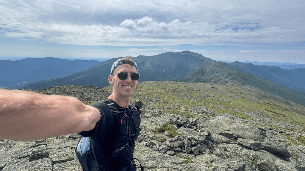 Selfie of a runner on Mount Jefferson during a presidential traverse in one day, with dramatic mountainous views and scattered clouds overhead.