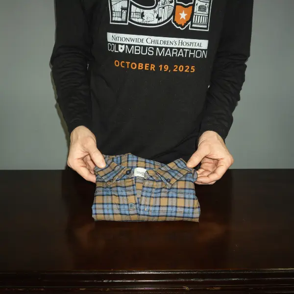 Neatly folded plaid shirt held at the corners, showing the end result of how to fold clothes for travel using the KonMari method.