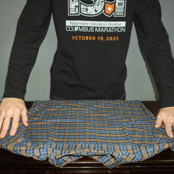 Blue and brown plaid shirt laid flat with sleeves spread, the starting step in how to fold clothes for travel.