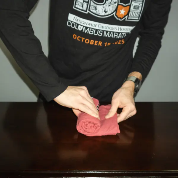 A red t-shirt tightly rolled into a compact cylinder, demonstrating the final step in rolling clothes for travel packing.