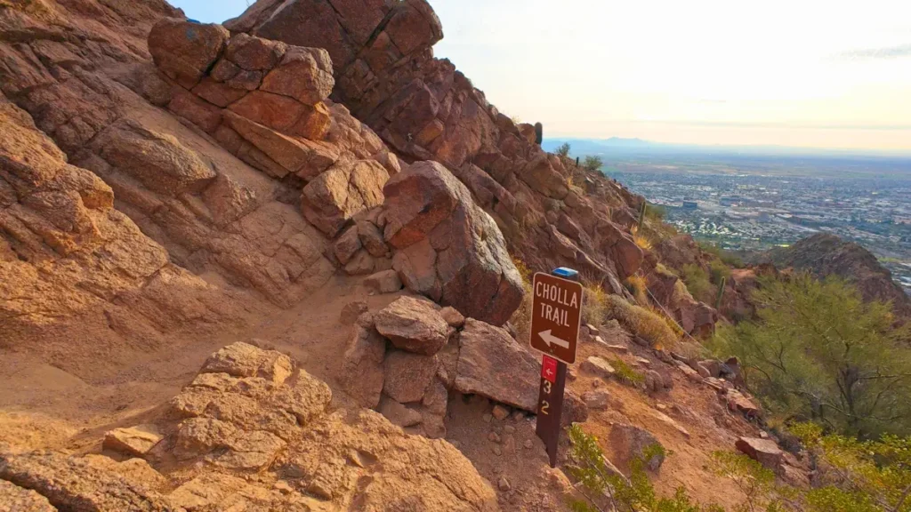 A close-up of the Cholla Trailhead wooden sign with rocky terrain in the background, marking a popular route for running Camelback Mountain.
