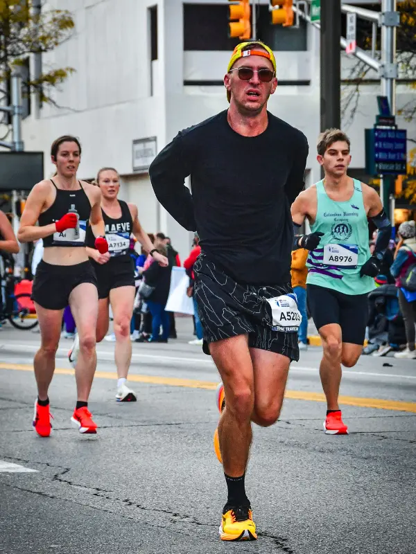 Kyle Cash racing through the streets of Indianapolis during the Monumental Marathon, wearing yellow Puma racing shoes and bib A5203, with other competitors close behind