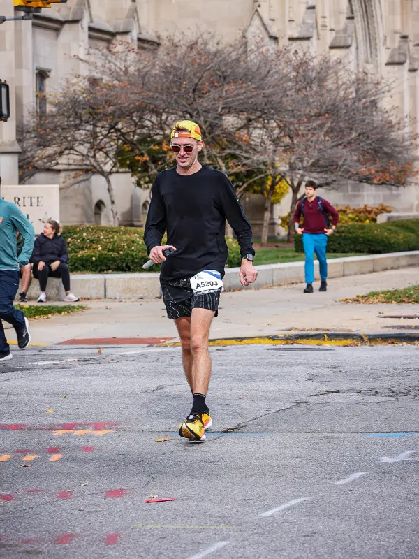 Kyle Cash smiling while running past a stone gothic building during the Indianapolis Monumental Marathon, wearing yellow racing shoes and a bright cap