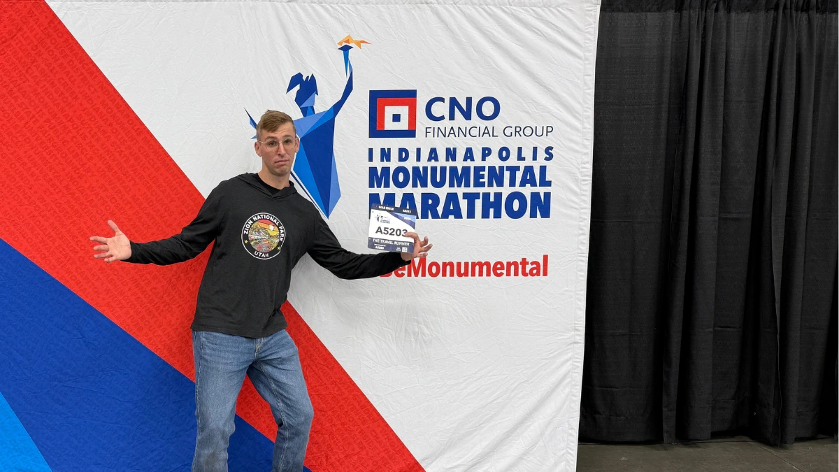 Kyle Cash posing at the Indianapolis Monumental Marathon expo, holding bib A5203 in front of the CNO Financial Group #BeMonumental backdrop