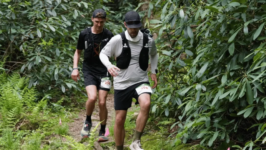 Two trail runners navigating a rocky, technical singletrack trail surrounded by dense green rhododendron bushes during the Rothrock by UTMB 50K race.