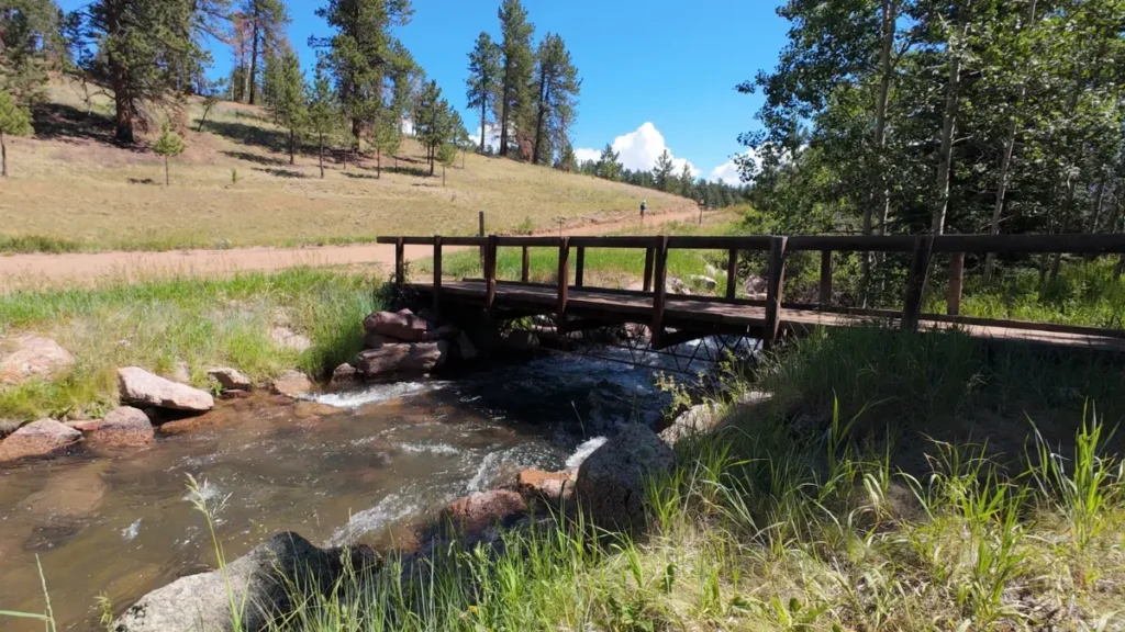 Wooden footbridge crossing a creek on the Rampart Reservoir trail, runner approaching in the distance