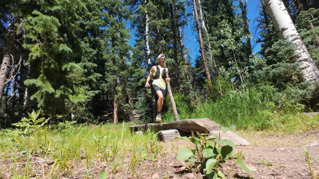 Runner crossing a log-and-plank bridge on singletrack through aspen and pine near Rampart Reservoir