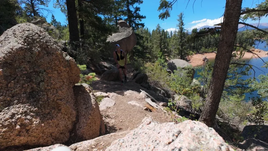 Runner climbing a rocky boulder section of the Rampart Reservoir trail above the water