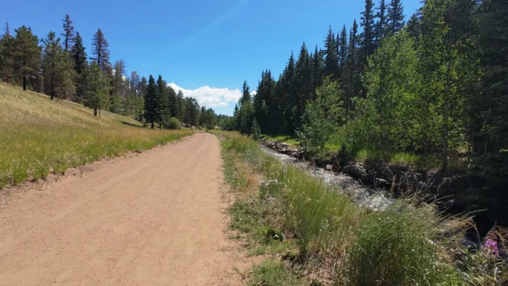 Wide gravel trail running alongside a creek on the approach to Rampart Reservoir