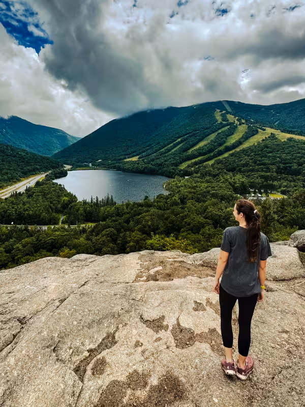 Kaitlyn stands on the rocky Artists Bluff viewpoint overlooking Echo Lake and Cannon Mountain in Franconia Notch.