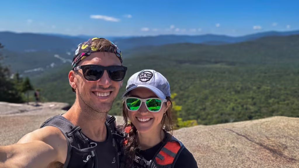 Kyle and Kaitlyn taking a selfie at Mount Pemigewasset’s viewpoint with forested ridges behind them.