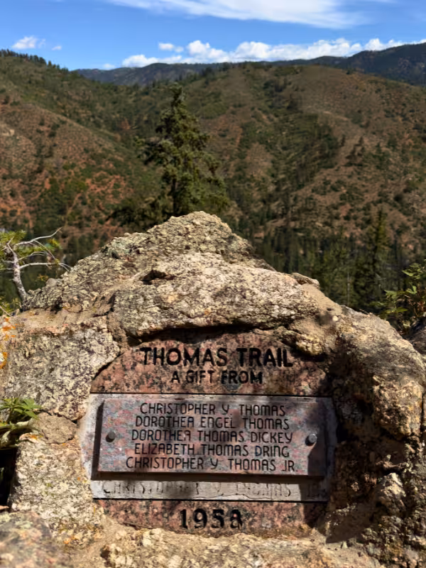 Thomas Trail dedication plaque set into a boulder above the forested hills near Green Mountain Falls.