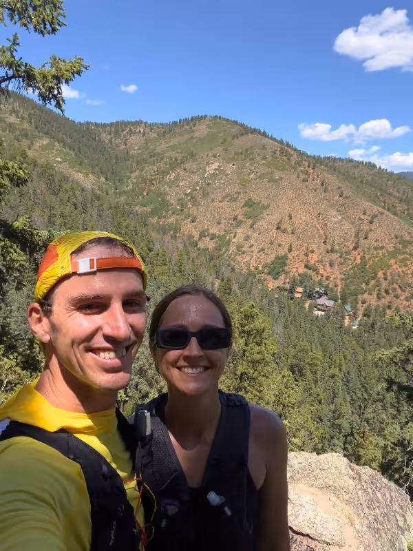 Two trail runners smiling at a rocky overlook above the forest near Green Mountain Falls.