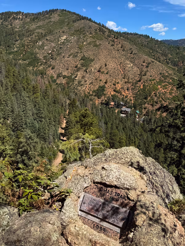 Thomas Trail dedication plaque on a boulder overlooking forested hills near Green Mountain Falls.