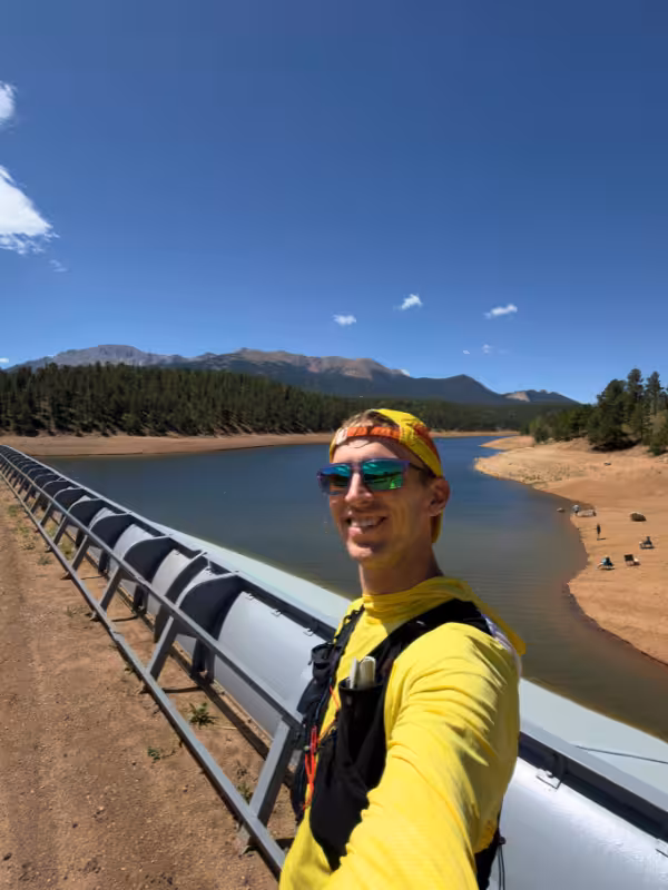 Trail runner beside South Catamount Reservoir, with the shoreline and mountains behind him.