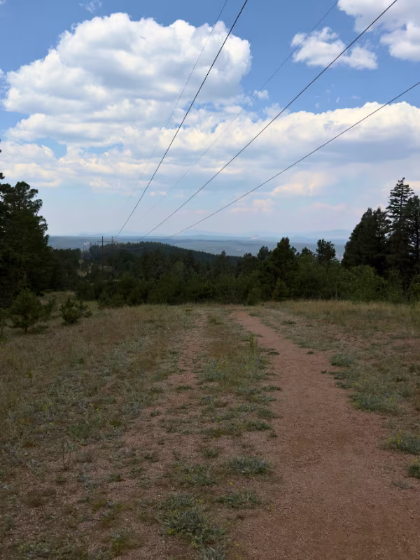Dirt trail crossing an open clearing beneath power lines, with distant mountain views along Lovell Gulch.